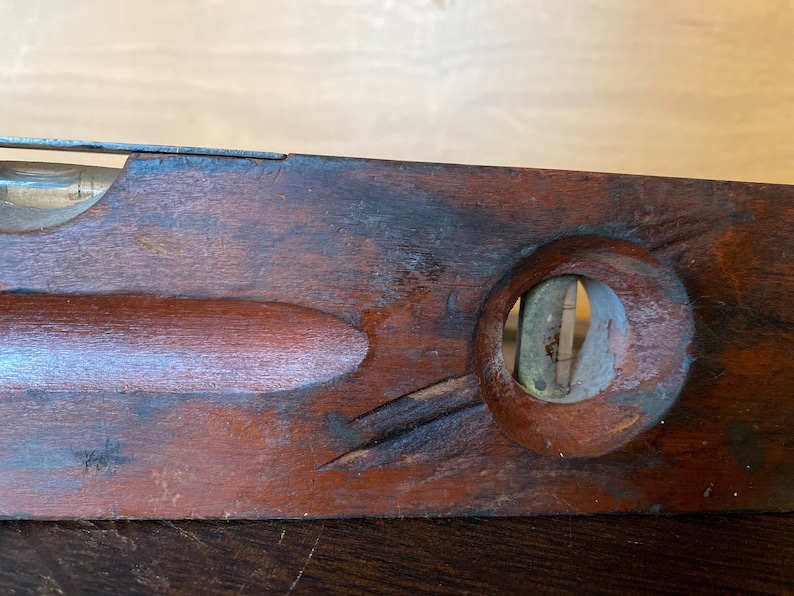 May include: A vintage wooden level with a brass bubble level. The level is dark brown and has a worn finish. The bubble level is circular and has a brass rim.