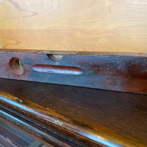 May include: A vintage wooden level with a brass level indicator. The level is dark brown and has a worn finish.