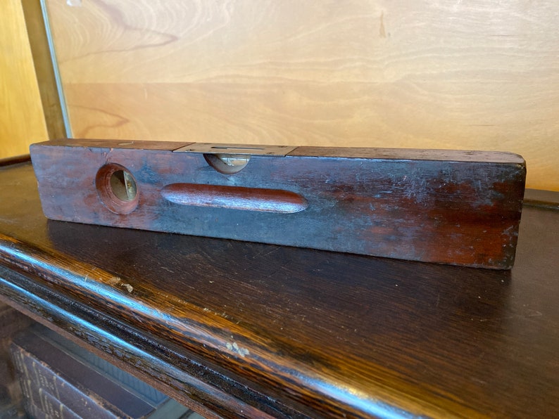 May include: A vintage wooden level with a brass level indicator. The level is dark brown and has a worn finish.