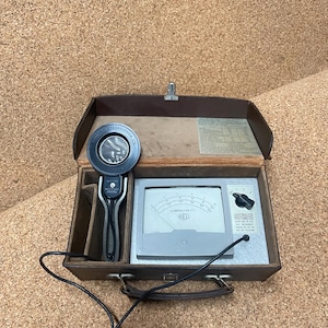 May include: A vintage EEL Lightmaster photometer housed in a brown carrying case. The device features a gray meter with a scale measuring Lumens/Sq Ft, a black dial, and a circular light sensor connected by a black cord. Text on the device includes Lightmaster Photometer and EEL.