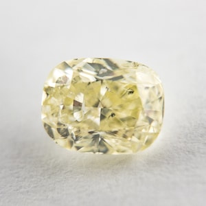 May include: A yellow cushion-cut diamond gemstone with a faceted surface.