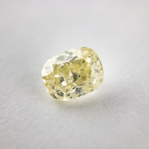 May include: A pale yellow, faceted gemstone with a cushion cut. The gemstone is set against a white background.