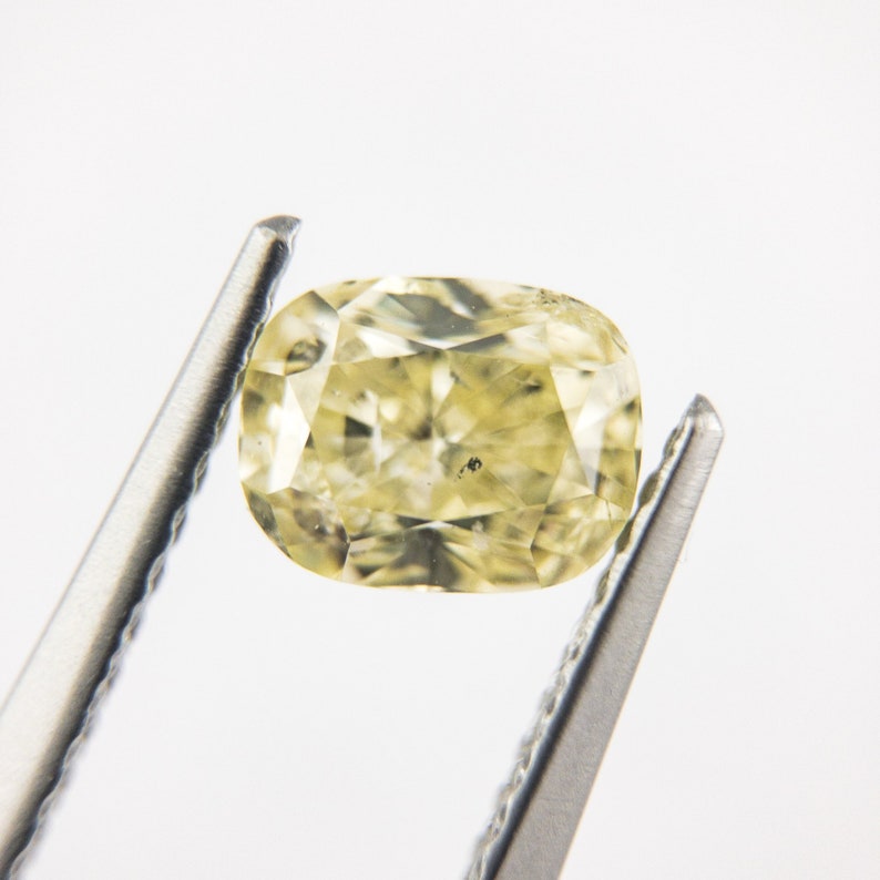 May include: A yellow oval-shaped gemstone held by tweezers. The gemstone has a faceted cut and is translucent.