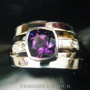 Könnte beinhalten: Mehrere Ringe, darunter einer mit einem großen, quadratisch geschliffenen, tiefvioletten Edelstein. Der Ring hat eine silberne Fassung, ein goldenes Band und kleine, klare Akzentsteine. Der Text "TRESORS DU JOUR" ist unten.