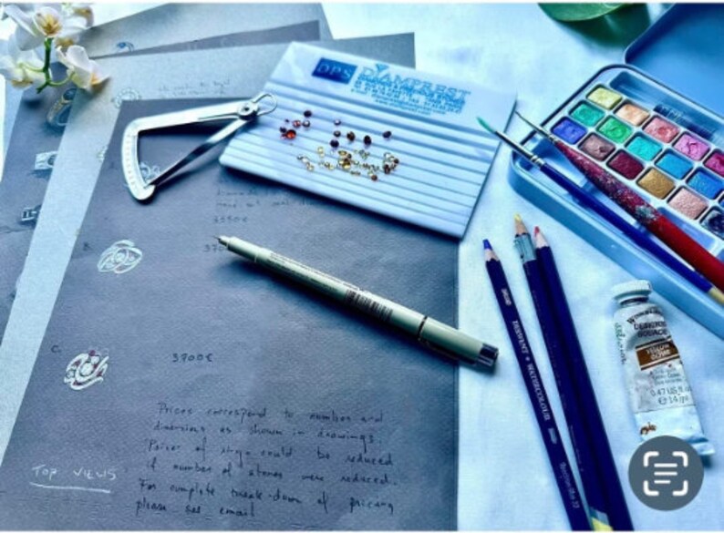 Op de afbeelding: Een werkruimte voor het ontwerpen van sieraden met een verscheidenheid aan gereedschappen en materialen.  Er zijn verschillende vellen papier met schetsen van sieradenontwerpen, een klein dienblad met edelstenen, een schuifmaat, een pen, een set kleurpotloden, een aquarelverfset en een tube verf.  De tekst op het papier luidt: "Prijzen komen overeen met het aantal en de afmetingen zoals weergegeven in de tekeningen.  Als het aantal stenen zou kunnen worden verminderd, zouden de prijzen in de fase kunnen worden verminderd.  Voor een volledige uitsplitsing van de prijzen, neem dan contact op via e-mail."