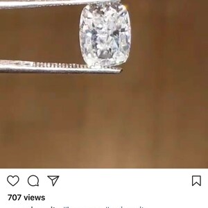 May include: A clear, cushion-cut gemstone, held by tweezers, is the focal point of this image. The gemstone has a crushed ice appearance, with a 9x12 mm size. The background is a warm, neutral tone, highlighting the brilliance of the gem.