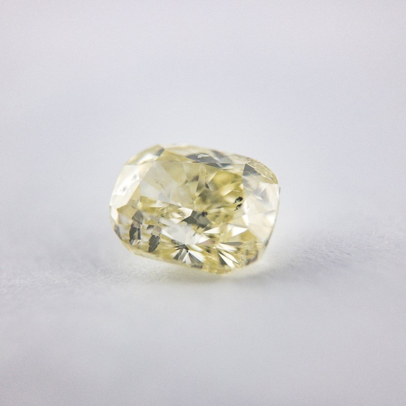 May include: A pale yellow cushion-cut diamond gemstone.
