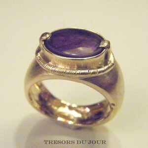 Op de afbeelding: Een zilveren ring met een ovale amethist edelsteen gezet in een bezel setting. De ring heeft een getextureerde band.