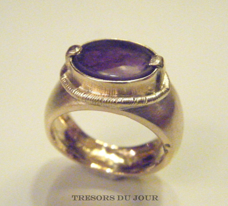 Op de afbeelding: Een zilveren ring met een ovale amethist edelsteen gezet in een bezel setting. De ring heeft een getextureerde band.