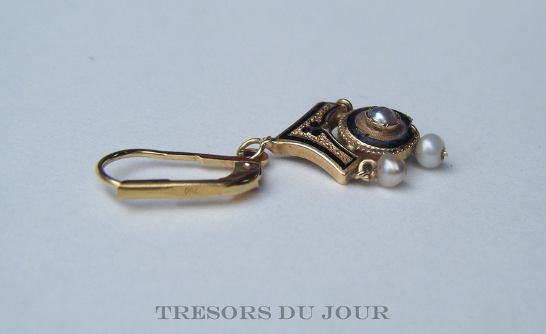 May include: Gold earring with a black enamel and pearl design. The earring has a hook closure and three pearls.