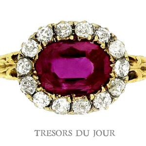 Peut inclure: Bague en or orn&eacute;e d'un rubis ovale entour&eacute; de diamants ronds. La monture de la bague pr&eacute;sente un motif floral. Le texte "TRESORS DU JOUR" est visible en bas de l'image.
