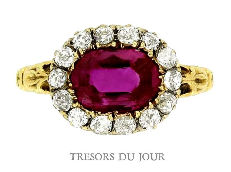 Peut inclure: Bague en or orn&eacute;e d'un rubis ovale entour&eacute; de diamants ronds. La monture de la bague pr&eacute;sente un motif floral. Le texte "TRESORS DU JOUR" est visible en bas de l'image.