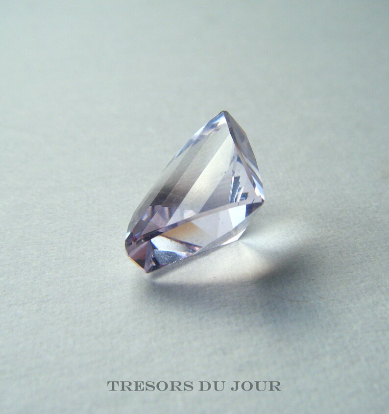 May include: A faceted amethyst gemstone with a light purple hue. The gemstone is cut into a unique shape with many facets.
