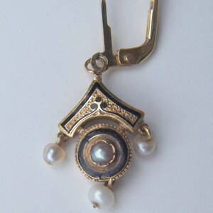 May include: Gold earring with a black enamel design and three white pearls. The earring has a lever back closure.