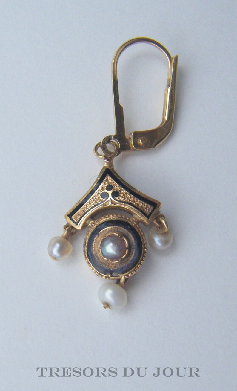 May include: Gold earring with a black enamel design and three white pearls. The earring has a lever back closure.