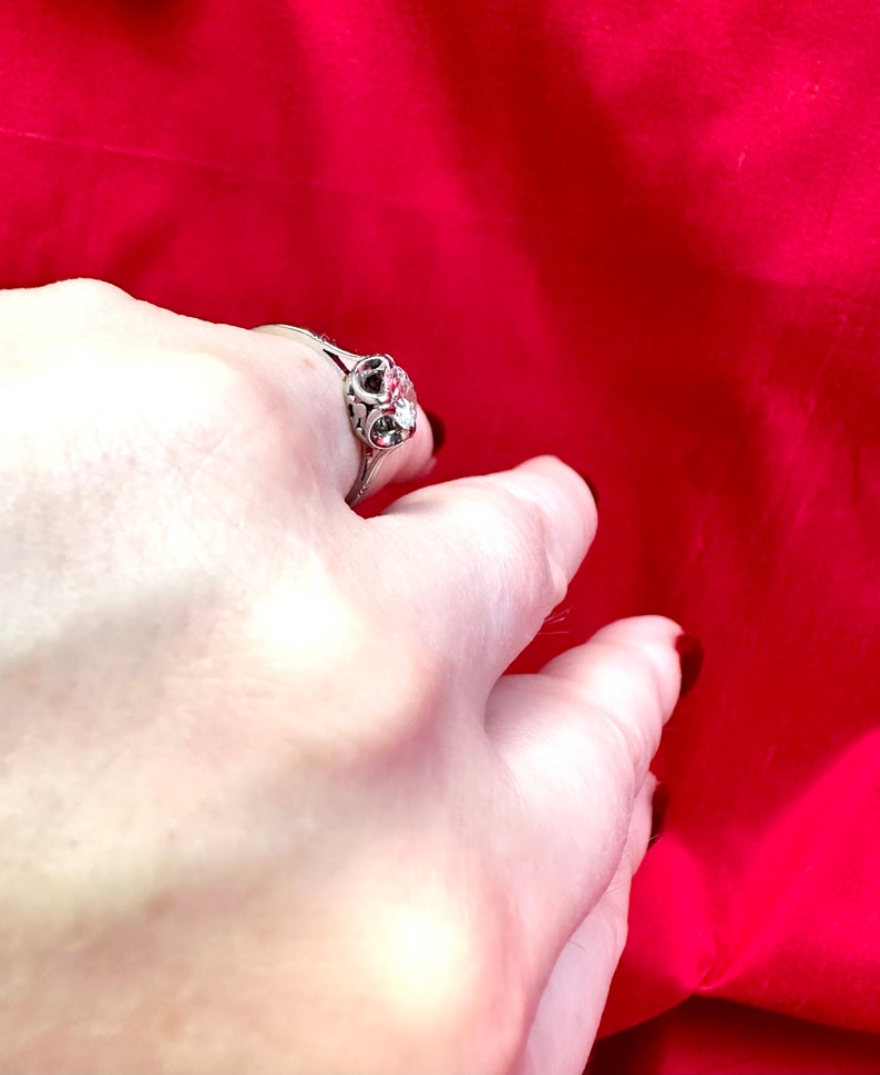 May include: A silver ring with a decorative filigree design and a central clear stone. The ring is set against a vibrant red background, creating a striking contrast. The ring's intricate details are visible.