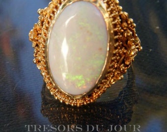 Puede incluir: Un anillo de oro con una piedra de ópalo ovalada engastada en un delicado diseño de filigrana.