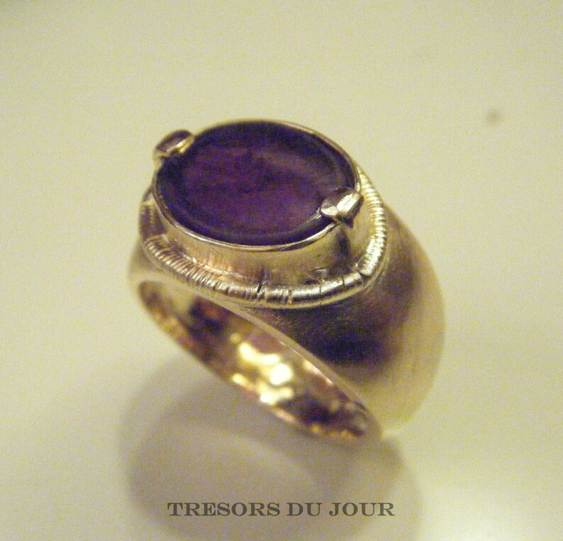 Op de afbeelding: Een gouden ring met een grote, ovale amethist edelsteen. De ring heeft een getextureerde band en een decoratieve zetting rond de steen.