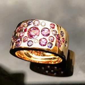 Può includere: Un anello con fascia in oro con una fascia larga e testurizzata incastonata con una varietà di pietre preziose colorate, tra cui rosa, viola, blu e bianco.