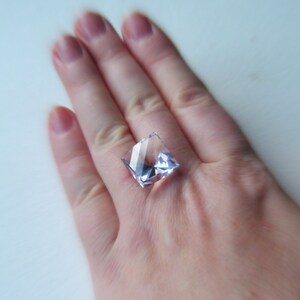 May include: A clear square-shaped crystal ring with a light purple hue.