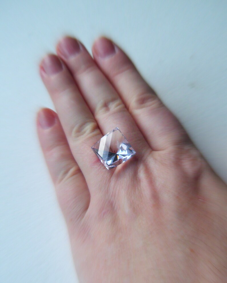 May include: A clear square-shaped crystal ring with a light purple hue.