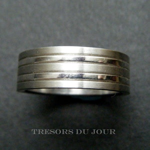 May include: A silver-toned ring with a series of horizontal grooves. The ring has a brushed metal finish and a simple, modern design. The ring is a band style, suitable for everyday wear.