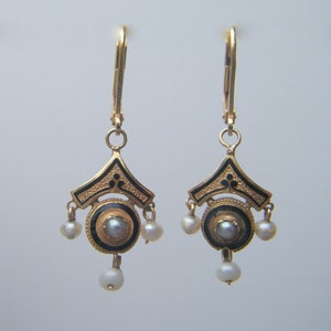 May include: A pair of gold earrings with black enamel and pearl accents. The earrings feature a geometric design with a central circle and dangling pearls.