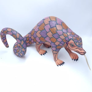 May include: A hand-carved wooden animal sculpture of a pangolin with a long tail. The sculpture is painted in shades of pink, orange, and green with intricate patterns.