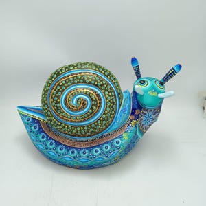 May include: A hand-painted, whimsical snail figurine. The shell is a spiral of green, gold, and blue dots. The body is a vibrant blue with intricate patterns. The snail's head is turquoise with detailed antennae. A unique decorative item.