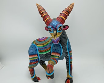 May include: A vibrantly painted wooden sculpture of an animal with large, spiraling horns. The artwork features intricate patterns in blue, red, yellow, and green. The animal stands on four legs, with a detailed design on its body.