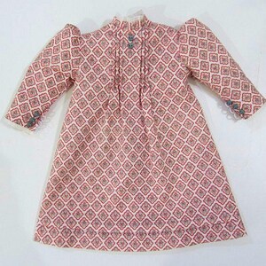 Pode incluir: Um vestido rosa e branco com um padr&atilde;o geom&eacute;trico. O vestido tem mangas compridas e gola alta. O tecido &eacute; macio e delicado.