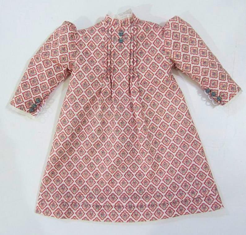 Pode incluir: Um vestido rosa e branco com um padr&atilde;o geom&eacute;trico. O vestido tem mangas compridas e gola alta. O tecido &eacute; macio e delicado.