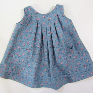 Pode incluir: Um vestido azul sem mangas com estampa floral e dois bolsos. O vestido tem uma saia franzida e um decote redondo.