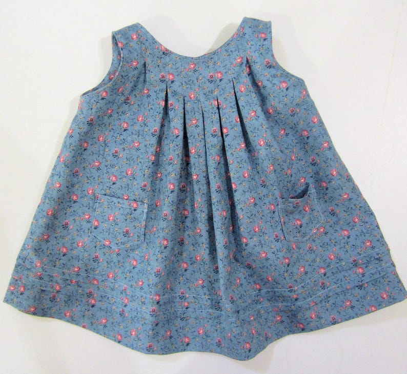 Pode incluir: Um vestido azul sem mangas com estampa floral e dois bolsos. O vestido tem uma saia franzida e um decote redondo.