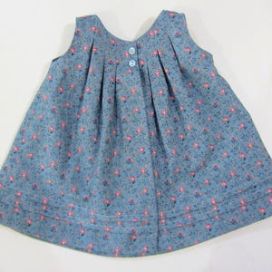 Pode incluir: Um vestido azul sem mangas com estampa floral e fecho de bot&atilde;o nas costas. O vestido tem pregas na frente e uma bainha de costura dupla.