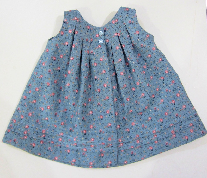 Pode incluir: Um vestido azul sem mangas com estampa floral e fecho de bot&atilde;o nas costas. O vestido tem pregas na frente e uma bainha de costura dupla.