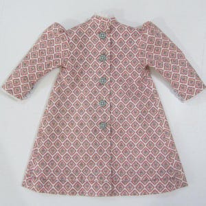 Pode incluir: Um vestido branco com padr&atilde;o rosa, com bot&otilde;es na frente e mangas bufantes.