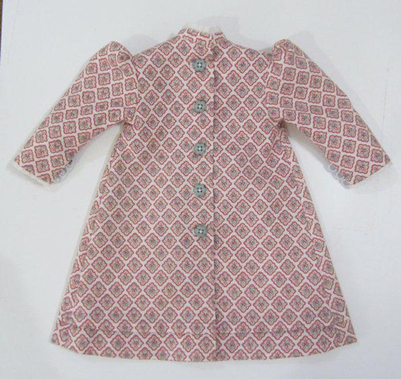 Pode incluir: Um vestido branco com padr&atilde;o rosa, com bot&otilde;es na frente e mangas bufantes.