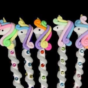 May include: Five unicorn-shaped pens with sparkly white bodies and colorful manes. The manes are pink, purple, orange, light blue, and green.