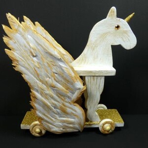 May include: A white wooden unicorn with gold wings and a gold horn. The unicorn has a white painted finish and is on wheels.