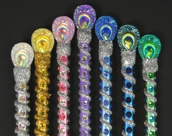 Puede incluir: Siete varitas decorativas con purpurina plateada y diseños de plumas de pavo real iridiscentes. Cada varita tiene una base de color diferente: morado, rosa, dorado, azul, verde, azul claro y verde azulado.