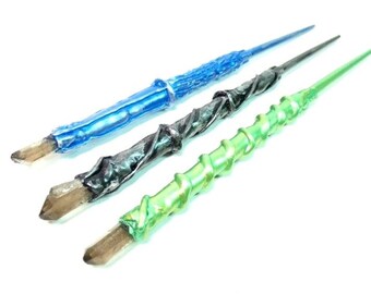 Puede incluir: Tres varitas decorativas con puntas de cristal. Las varitas están hechas de diferentes materiales y colores, incluyendo azul, verde y negro.