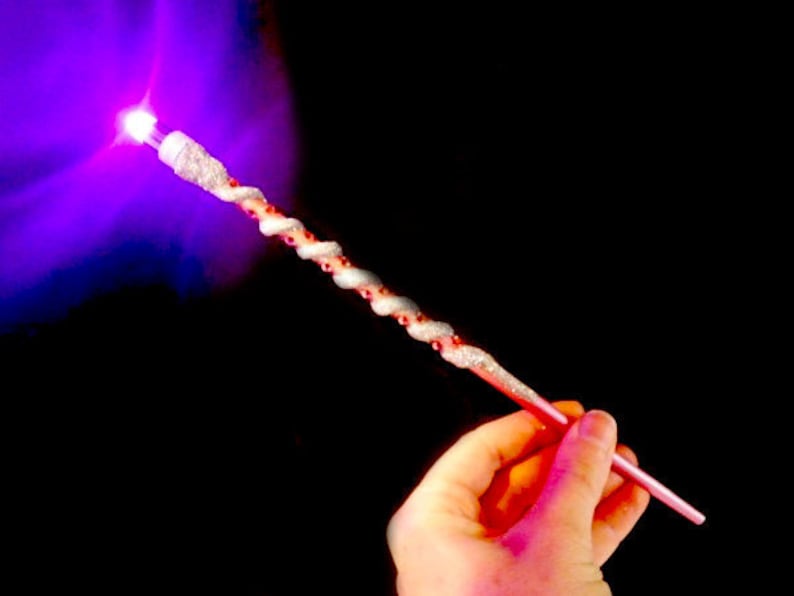 May include: A white and pink wand with a sparkly finish and a purple light at the tip.