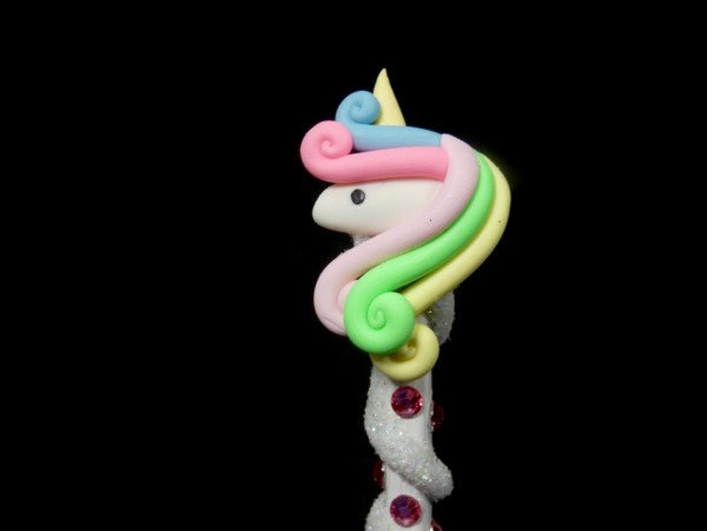 May include: A white unicorn head with a rainbow mane and a pink horn. The unicorn head is attached to a white stick with pink glitter.