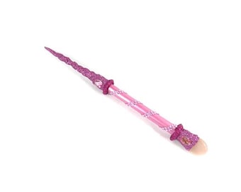 May include: A pink and glittery unicorn wand with a spiraled design. The wand features a pink handle with a spiral of small, white beads. The tip is a light pink color, and the wand is decorated with pink glitter.