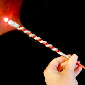 May include: A red and white twisted wand with a glowing light at the tip. The wand is held in a hand.