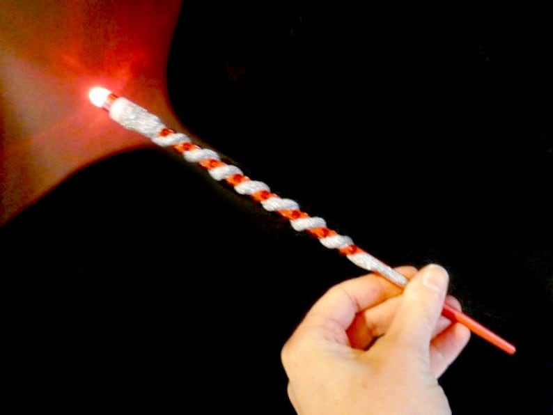 May include: A red and white twisted wand with a glowing light at the tip. The wand is held in a hand.