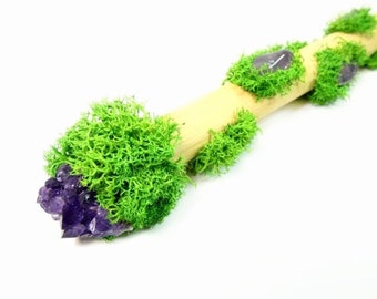 May include: A wooden wand with green moss and amethyst crystals. The wand is decorated with moss and crystals, creating a natural and magical look.