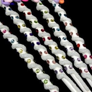 May include: Six white, sparkly, twisted wands with colorful rhinestones. Each wand has a different color of rhinestones, including red, green, blue, purple, pink, and yellow.