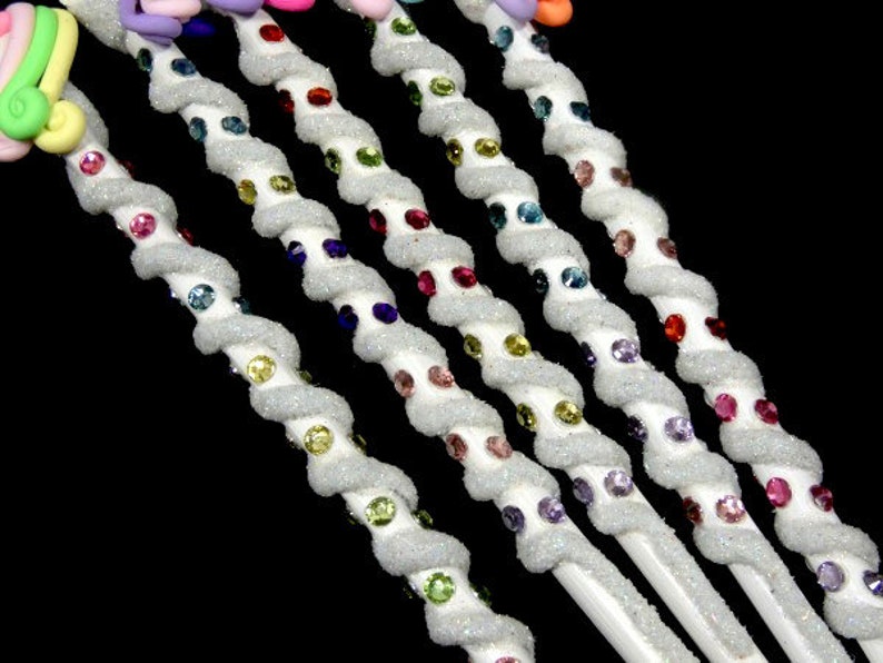 May include: Six white, sparkly, twisted wands with colorful rhinestones. Each wand has a different color of rhinestones, including red, green, blue, purple, pink, and yellow.